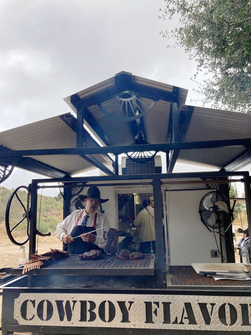 Billy turning beef on the grill at the back of the white cook trailer