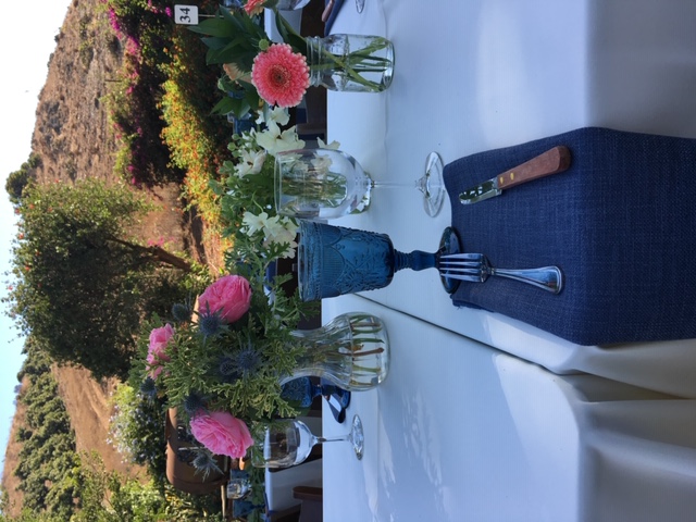 pink flowers in vases on white tablecloth. blue glasswear and napkin with steak knife and fork.