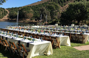 Multiple tables set up for outdoor wedding reception overlooking a lake.