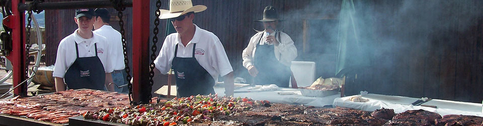 two cooks flipping meat on grill