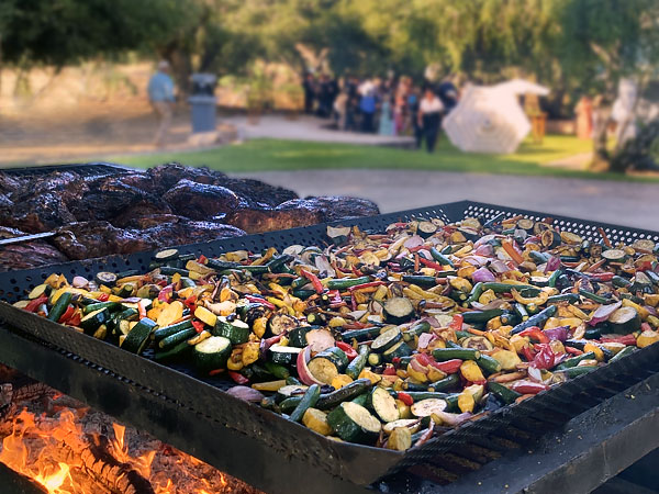 Closeup of grill with beef and vegetables and party in the background