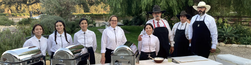 five female servers, Billy and two pit masters standing at a table of food